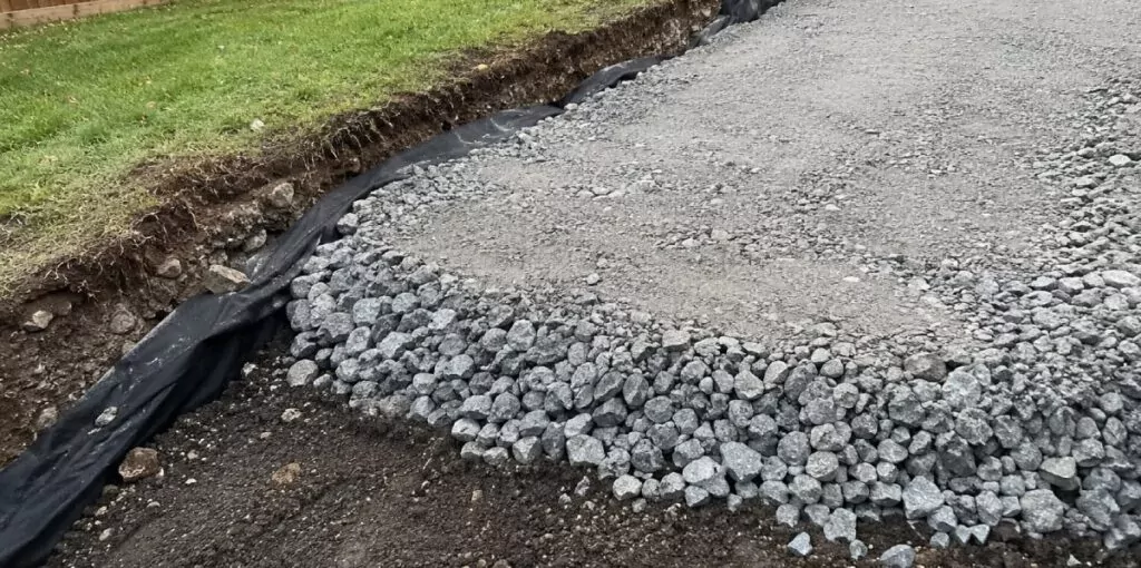 Layered crushed stone base in excavated gravel driveway trench