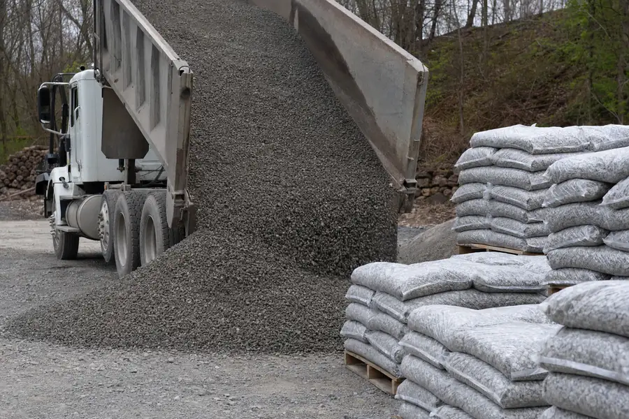 Delivery truck dumping crusher run gravel beside stacked bags of 57 stone