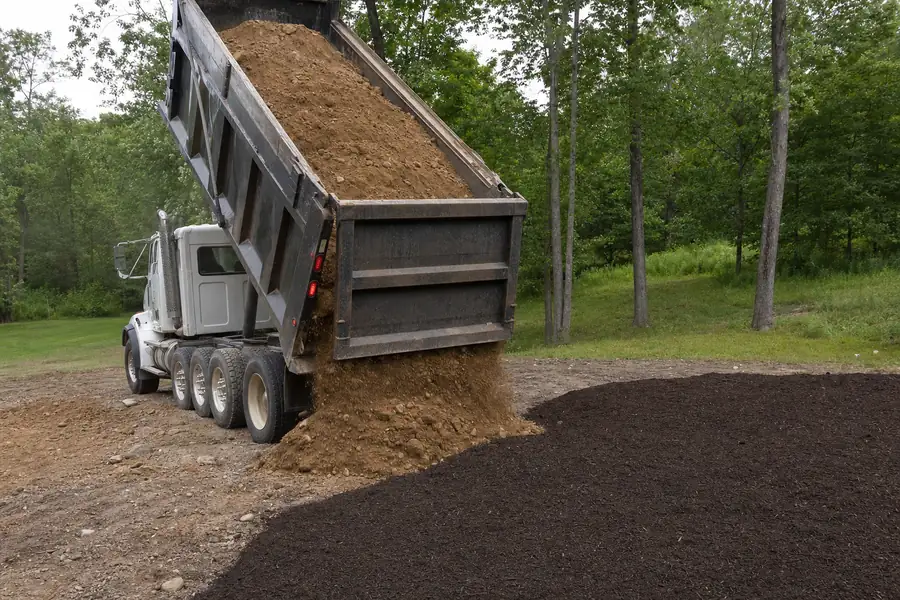 Dump truck delivering fill dirt beside a finished bed of dark topsoil