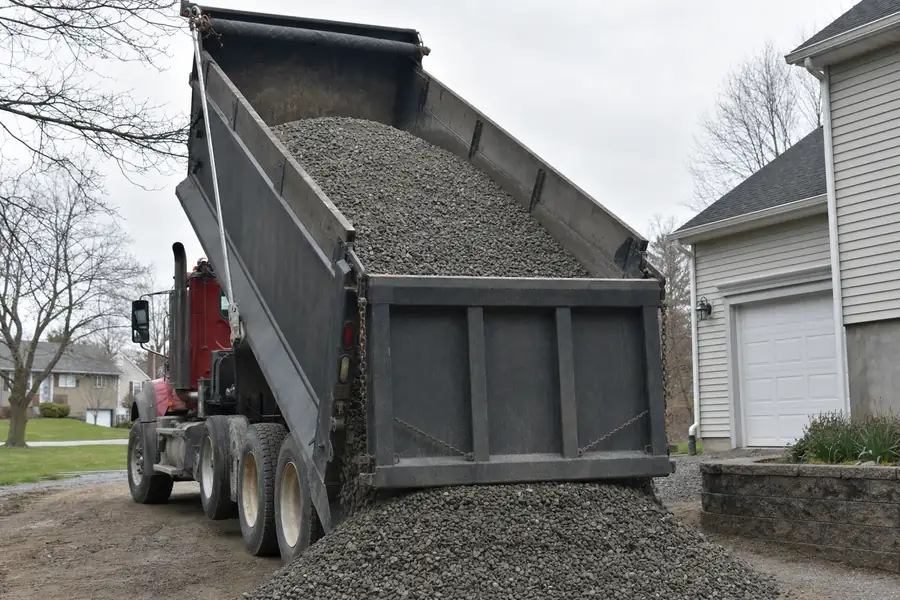 Dump truck tipping a load of crushed gravel into a residential driveway