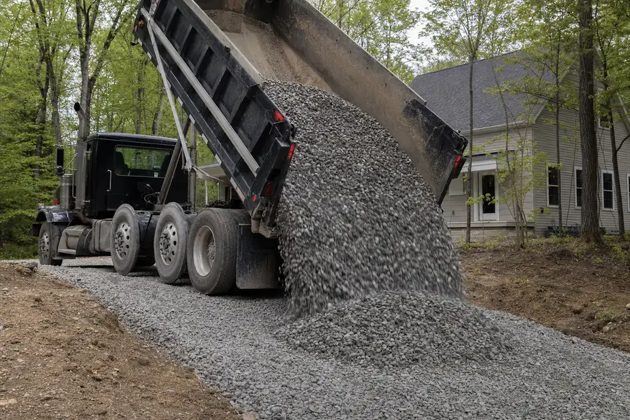 Gravel truck dumping crushed stone onto a new residential driveway base