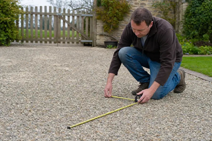 Homeowner measuring a gravel driveway area with a tape measure