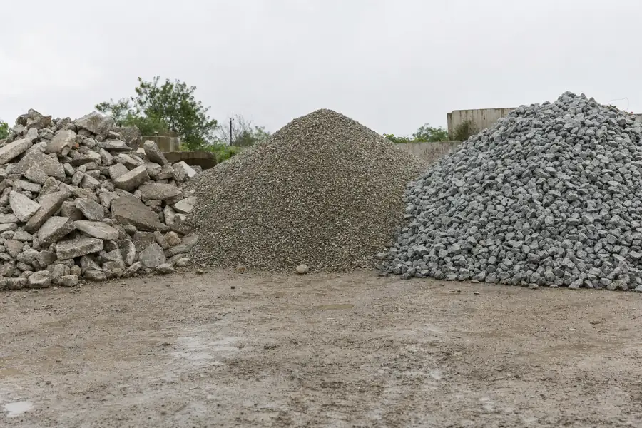 Side by side stockpiles of crushed concrete, gravel, and crushed stone at a supply yard