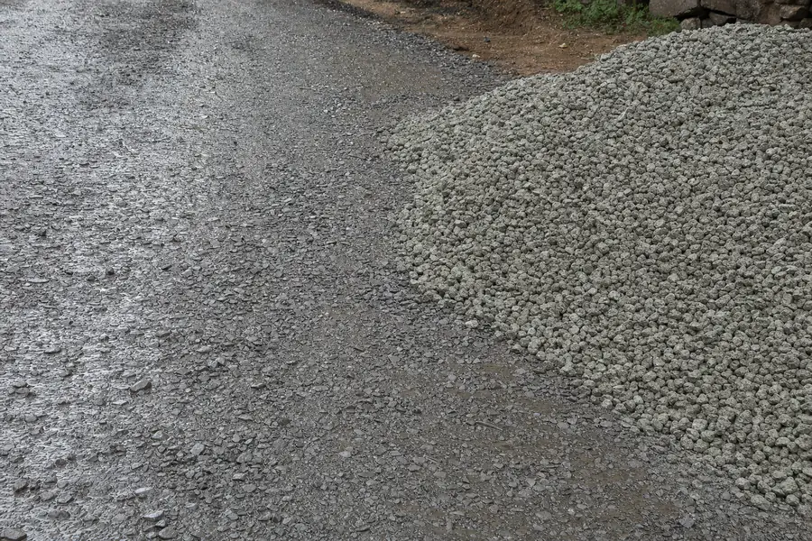 Wet crushed gravel driveway base glistening after rainfall next to dry stockpile
