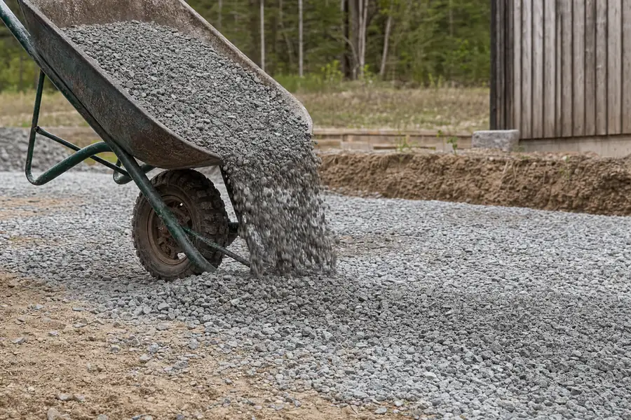 Wheelbarrow load of crushed concrete being spread over a compacted driveway base