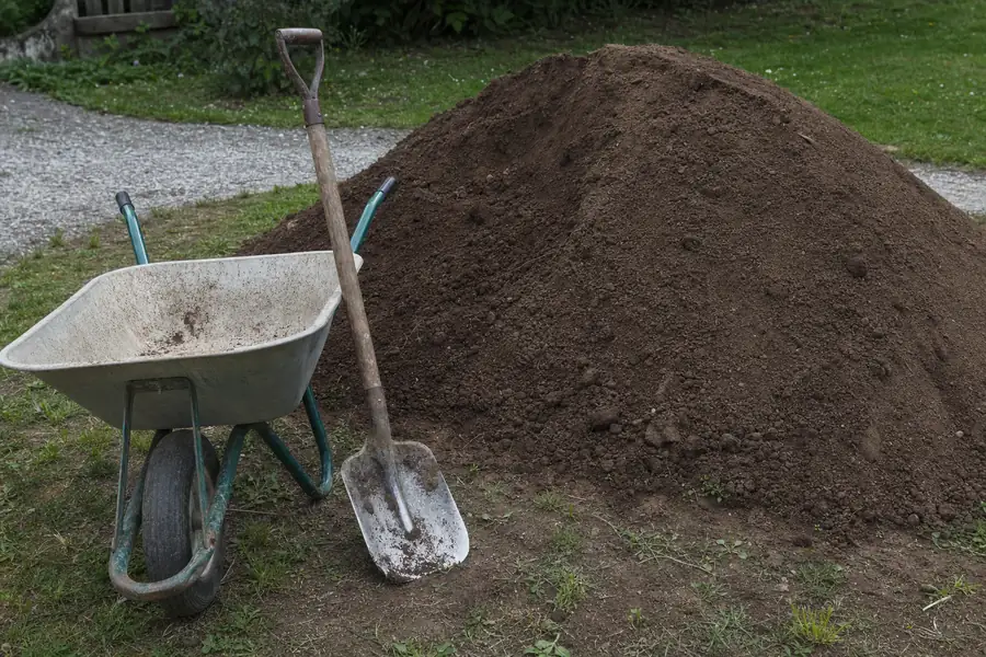 Wheelbarrow and shovel beside a freshly delivered mound of clean fill dirt in a yard