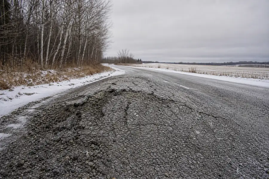 Frost-heaved rural road surface showing a raised hump and cracked crown under grey winter sky