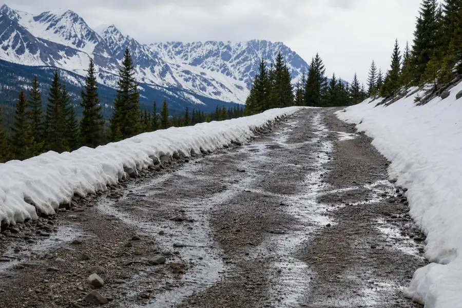 Snowmelt running down a sloped gravel driveway with the Rocky Mountains visible behind
