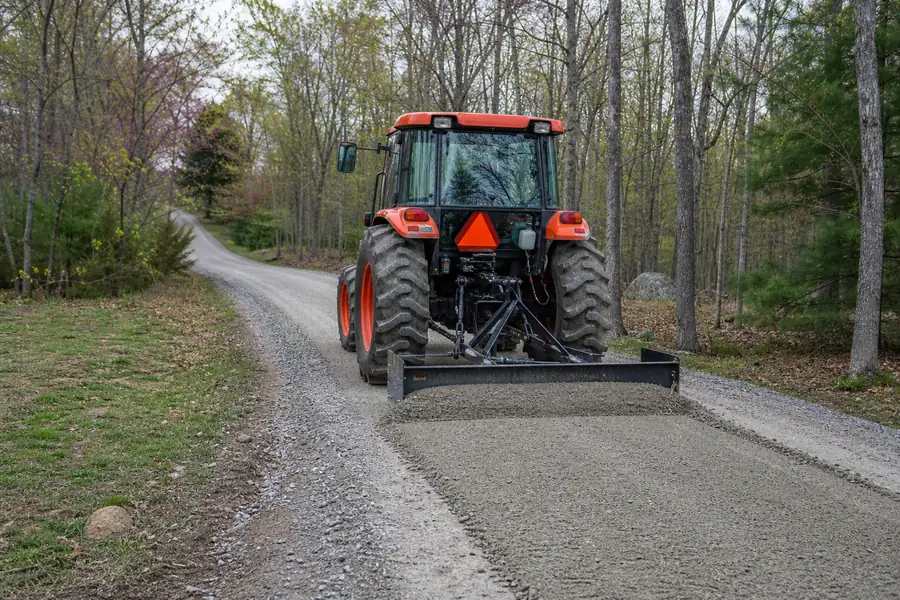 Tractor with a box blade regrading a gravel driveway in spring, fresh crown visible